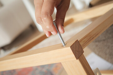 Hand holds a screw while assembling wooden furniture piece
