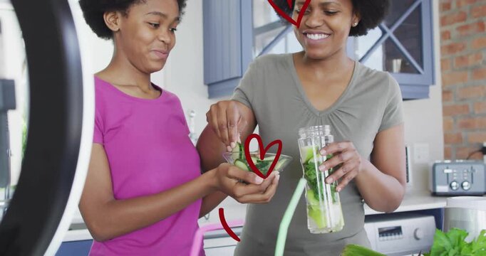 Mother and daughter making health drink at counter, phone recording content, hearts overlaying jar