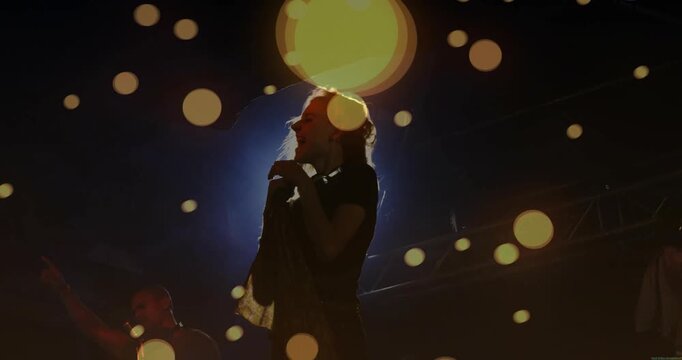 Lead singer whipping hair gripping mic settling singing music as bokeh drifting and light flaring