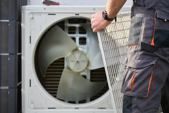 Technician removing front cover grille from outdoor heat pump unit during residential HVAC service. Concept of heat pump maintenance repair and home heating and cooling