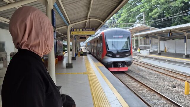 A Muslim woman wearing a hijab waits for the arrival of a modern commuter train