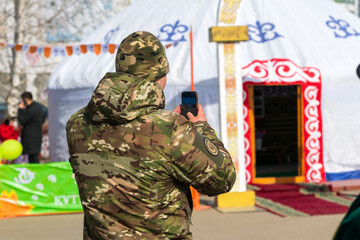 Fototapeta premium Man in camouflage jacket taking photo of traditional Kazakh yurt during Nauryz celebration