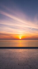 Fototapeta premium Golden sunset over calm ocean reflecting vibrant sky with wispy clouds, viewed from a modern terrace with glass railing.