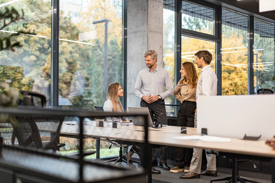 Happy four business people executive team working at laptop having discussion at office meeting showing financial project