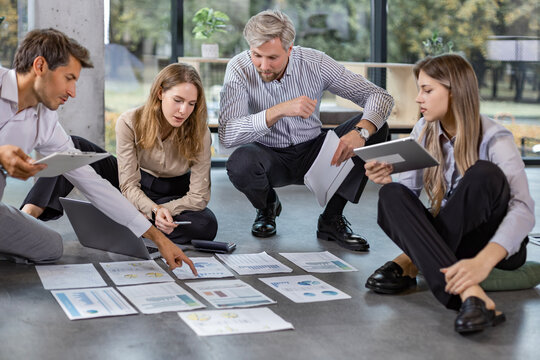 Group of young business people working on new project sitting with financial documents spread out on the floor