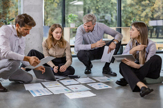 Young business people in a meeting working together on a creative financial project laid out on floor