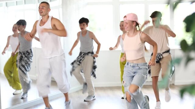 Happy teenage children and young male trainer practicing hip-hop reject steps during workout session in group. High quality 4k footage