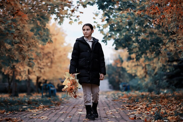 Fototapeta premium Woman Walking Through Autumn Park Holding Leaves, Enjoying Nature