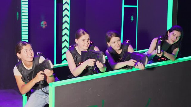  Portrait of excited girlfriends playing enthusiastically laser tag game two teams opposite each other in dark room