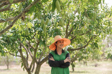 Female mango farmer standing arms crossed in tropical orchard show successful organic fruit harvest...