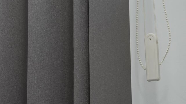 The curtain is being opened using a pull cord mechanism. The room has natural light coming in through the curtain. The setting is simple and modern.