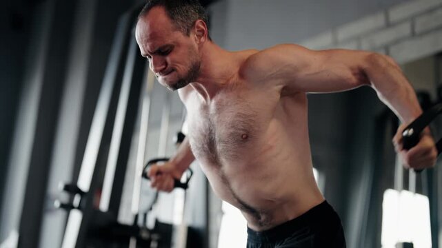 Determined bodybuilder with a muscular physique doing a chest workout using a cable crossover machine in the gym, showcasing intense effort and concentration during his strength training session