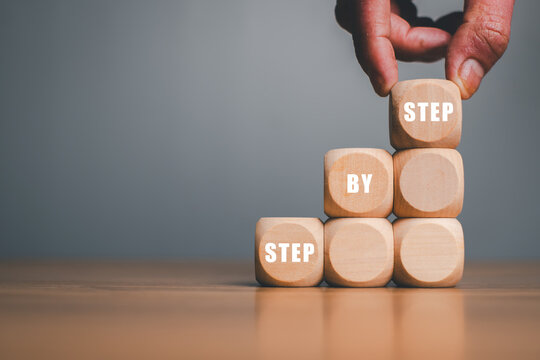 Hand placing wooden blocks with "Step by Step" text, symbolizing progress, growth, and success in business or personal development.