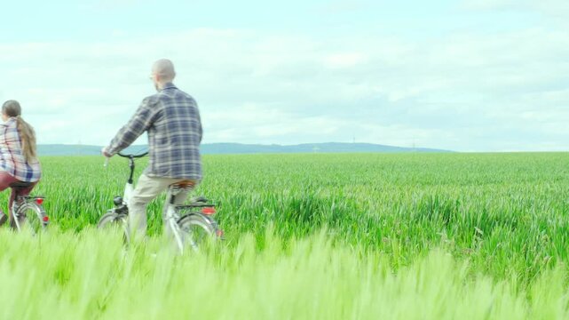 Pedaling expanse swaying green wheat fields, mature family with an adult son riding bicycles together, beauty rural landscape, rustic beauty, journey metaphor life's path