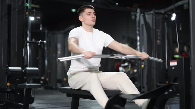 Focused young man maintaining active healthy lifestyle, working out back muscles on seated cable row machine in modern gym environment, building strength and posture. High quality 4k footage
