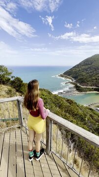 Woman traveler standing on viewing platform at Teddy&rsquo;s Lookout, admiring the view of the outlet river and turquoise ocean and surrounding hills, near Lorne, Melbourne, Victoria, Australia
