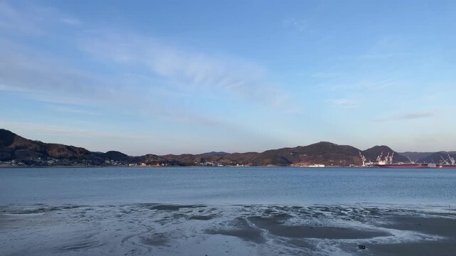 A calm coastal scene in the Seto Inland Sea, Japan. Gentle waves move quietly under soft natural light, with a peaceful island landscape in the distance. The atmosphere is still and minimal, capturing