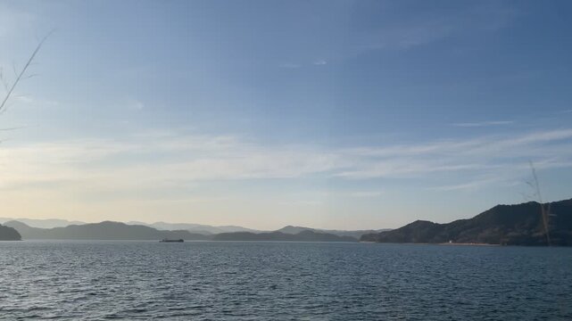 A calm coastal scene in the Seto Inland Sea, Japan. Gentle waves move quietly under soft natural light, with a peaceful island landscape in the distance. The atmosphere is still and minimal, capturing