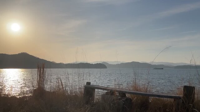 A calm coastal scene in the Seto Inland Sea, Japan. Gentle waves move quietly under soft natural light, with a peaceful island landscape in the distance. The atmosphere is still and minimal, capturing