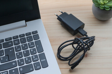 Fototapeta premium Laptop and charger resting on a wooden desk, symbolizing modern workspace setup for students, remote workers, and adapting to hybrid employment models