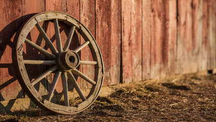Fototapeta premium Old wooden wagon wheel rests against barn wall at a farm in the late afternoon light