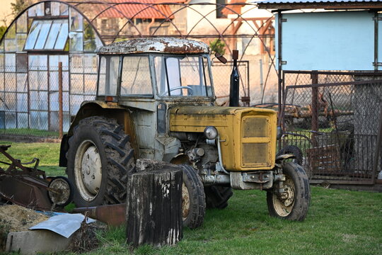 Old tractor with rusty cabin and yellow hood in rural farm setting

