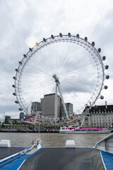 Fototapeta premium London, United Kingdom, 13 July 2023, The London Wheel rises above the Thames in central London. A river vessel passes below the wheel during daytime.