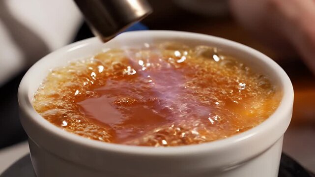Close-Up Of White Sugar Being Caramelized With A Kitchen Torch To Create A Golden Brown Crust On A Creme Brulee Dessert In A White Ramekin