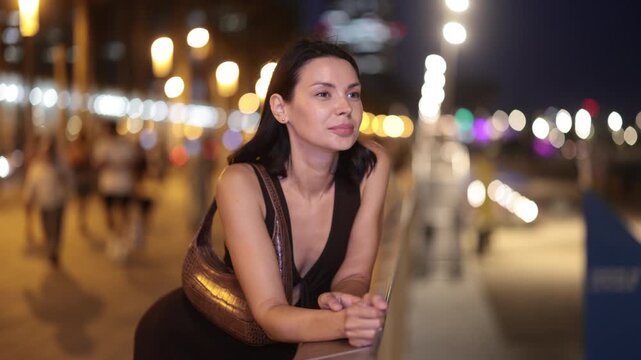 Night walk around old district. Woman put hands on fencing, watching towards beach of Barceloneta from height of pedestrian promenade. Night fell on city