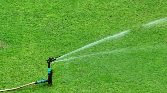 Drone perspective of a well-maintained lawn being irrigated by a sprinkler, representing modern water distribution systems, sustainability, the importance of consistent hydration for green landscapes.