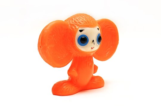 Bright orange Cheburashka figurine with large ears, big blue eyes, and a small smile, standing on a white background.