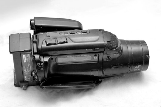 Black, vintage Sony video camera recorder with control buttons, lens, and hand strap, lying on a white surface, showcasing retro technology - October 22, 2020, Saint Petersburg, Russia.