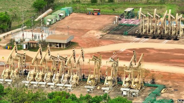 Aerial drone view of multiple oil pumpjacks aligned in a vast dry field, showcasing large-scale petroleum extraction, industrial energy production, and the backbone of global oil supply systems.
