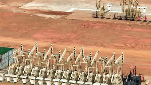 Overhead drone view of oil pumpjacks in a structured row, representing large-scale crude production, economic influence of oil markets, and ongoing global reliance on petroleum resources.
