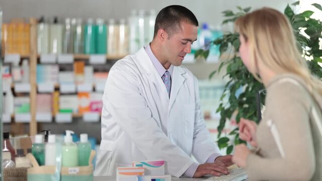 Qualified male pharmacist works with a client's order and checks the availability of medicines on a computer. Female buyer consults with a pharmacy employee about the choice of medicines. High quality