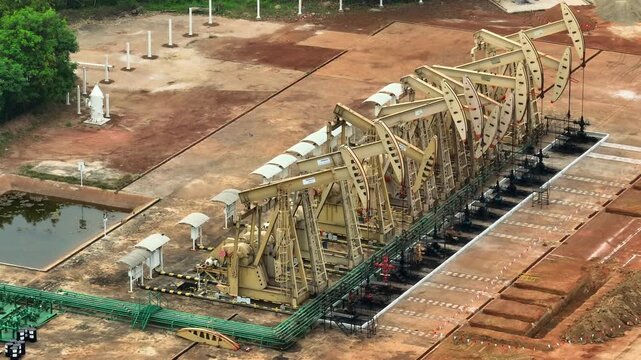 Drone perspective capturing rows of active oil pump jacks, symbolizing current global oil production, price volatility, and the balance between traditional energy and the transition toward renewables.