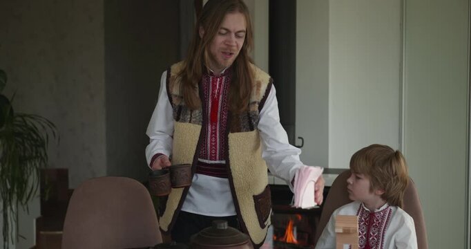 Kid Boy Waiting For Dinner. Man Serving Dishes on Table Family in Ukrainian Traditional Attire Childhood. 4K 10-bit