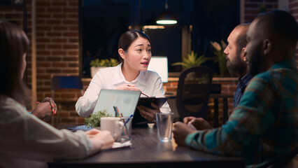 Obraz premium Asian woman speaking financial report in business meeting, employee discussing corporate presentation at table. Coworkers brainstorming, company marketing research analytics discussion