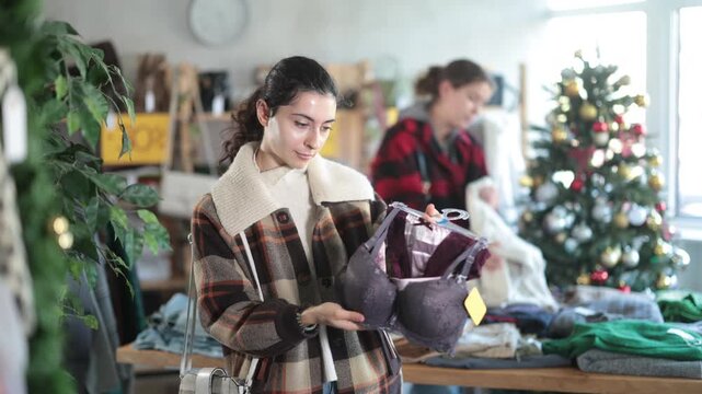 Armenian woman chooses a bra based on the materials comfort and prefers seamless styles. Shopper stands in a clothing store with a Christmas tree in the background, buying lingerie. High quality 4k