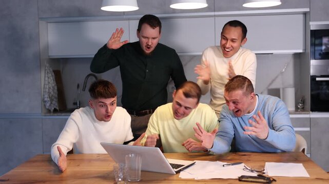Group of men watching sports match online on laptop during friendly meeting with beer at home, excitedly celebrating winning score in game 