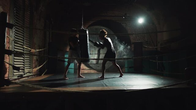 Active lifestyle and professional sport, athletic woman training in box club. People on boxing ring in darkness, young african man and woman practicing arms punches, self-defense class for ladies