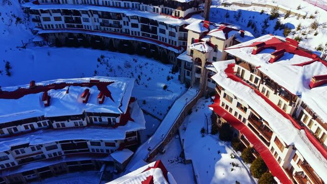 Winter scene shows buildings covered in snow at a mountain resort. Snow blankets the roofs and grounds, creating a white landscape. The layout includes walkways and structures.