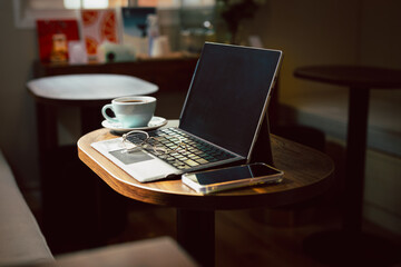 Fototapeta premium Cozy cafe workspace with tablet, coffee cup, glasses, and smartphone on a wooden table.