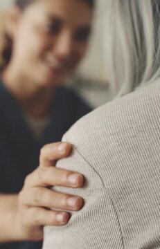 Healthcare worker touching elderly patient's shoulder with compassion and talking