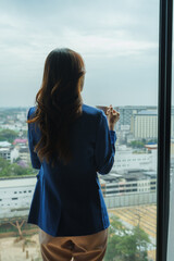 Fototapeta premium Woman holding cup looking out city window