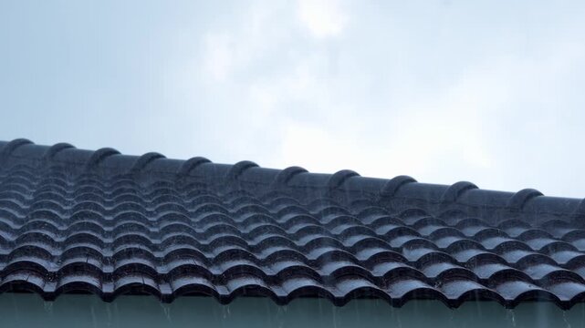Heavy rain pouring over a tiled roof, highlighting extreme weather intensity, climate change impacts, and increasing rainfall patterns linked to global warming and environmental instability.
