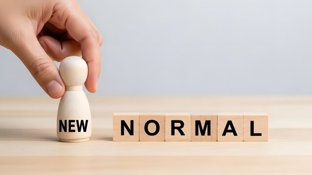Hand places a wooden figure on blocks spelling new normal on a clear surface