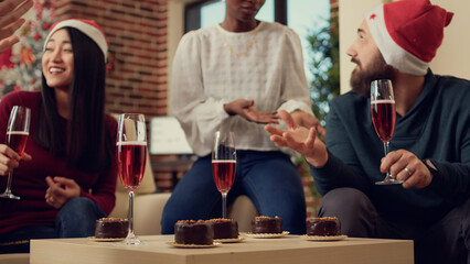 Naklejka premium Diverse people drinking glasses of wine at holiday festivity in office with xmas decorations. Serving alcoholic beverage to celebrate christmas eve party with presents and festive decorations.