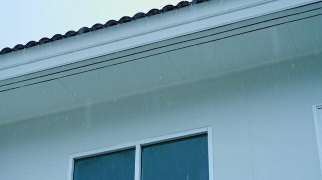 A rainfall falling along a residential rooftop, illustrating shifting climate conditions, unpredictable storms, the growing influence of global warming on everyday environments and weather extremes.
