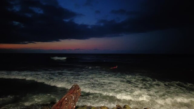 Panoramic view of a person on a surfboard on the beach along the Choroni boardwalk at night, looking out to sea at sunset, Aragua, Venezuela
